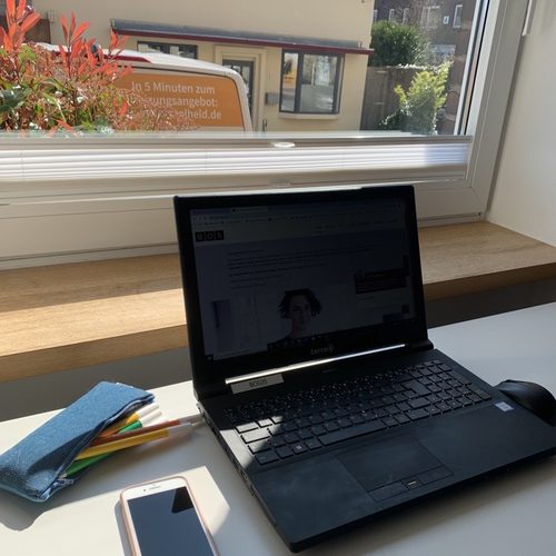 Bild vom sporadischen Arbeitsplatz mit Laptop und Handy am lichtdurchfluteten Fenster.