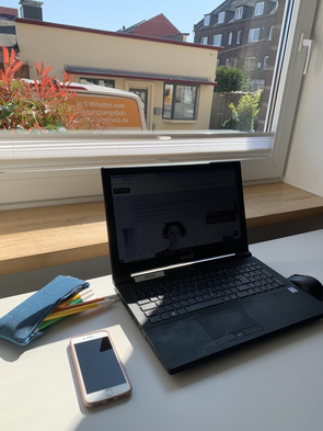 Bild vom sporadischen Arbeitsplatz mit Laptop und Handy am lichtdurchfluteten Fenster.